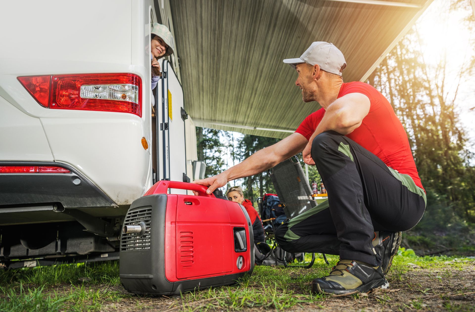 Man starting a red generator next to a white RV, person looks out the door, sunny outdoor setting.