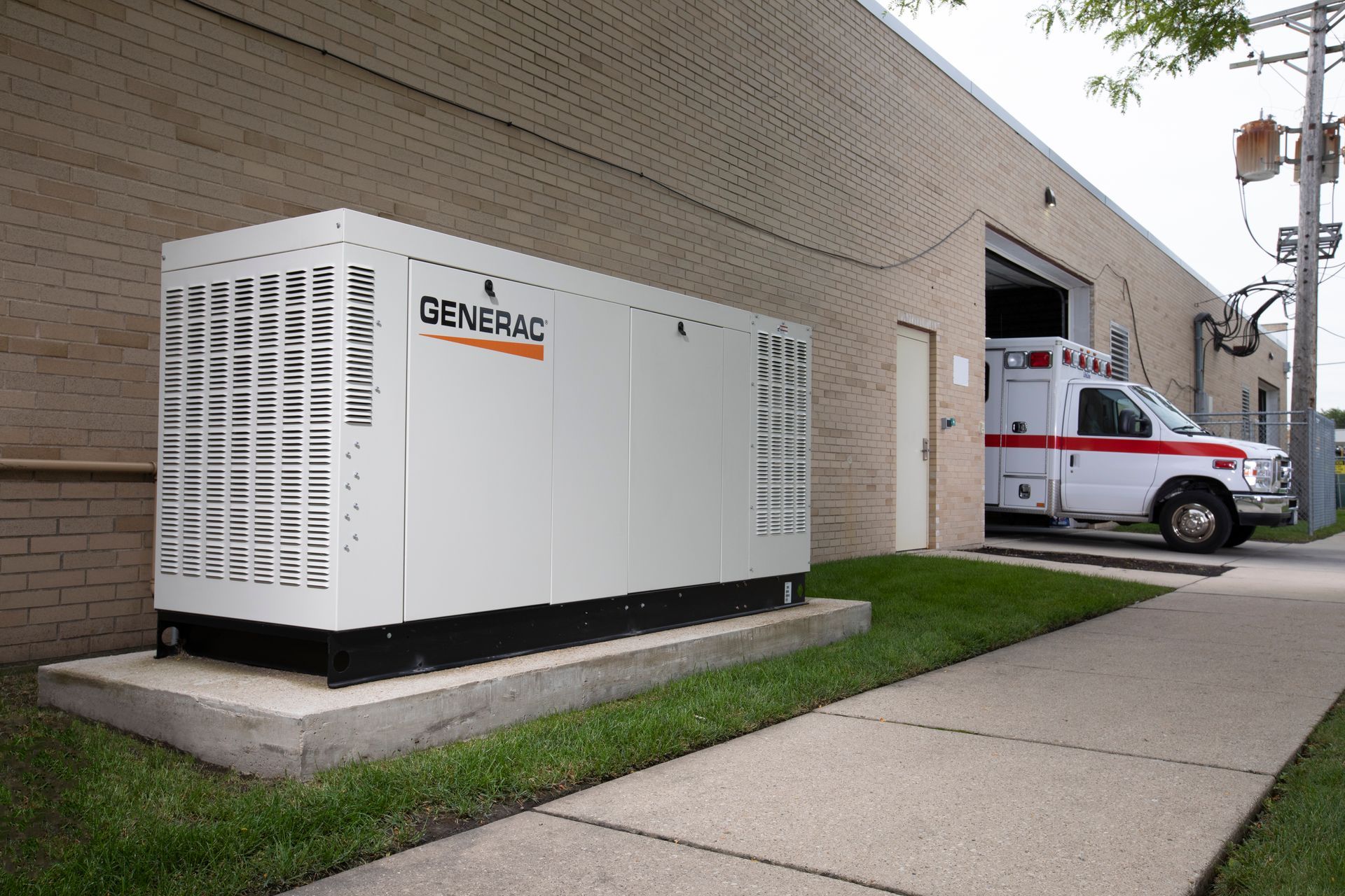 Generator in front of a tan house with a red-tiled roof, flanked by green bushes and a driveway.