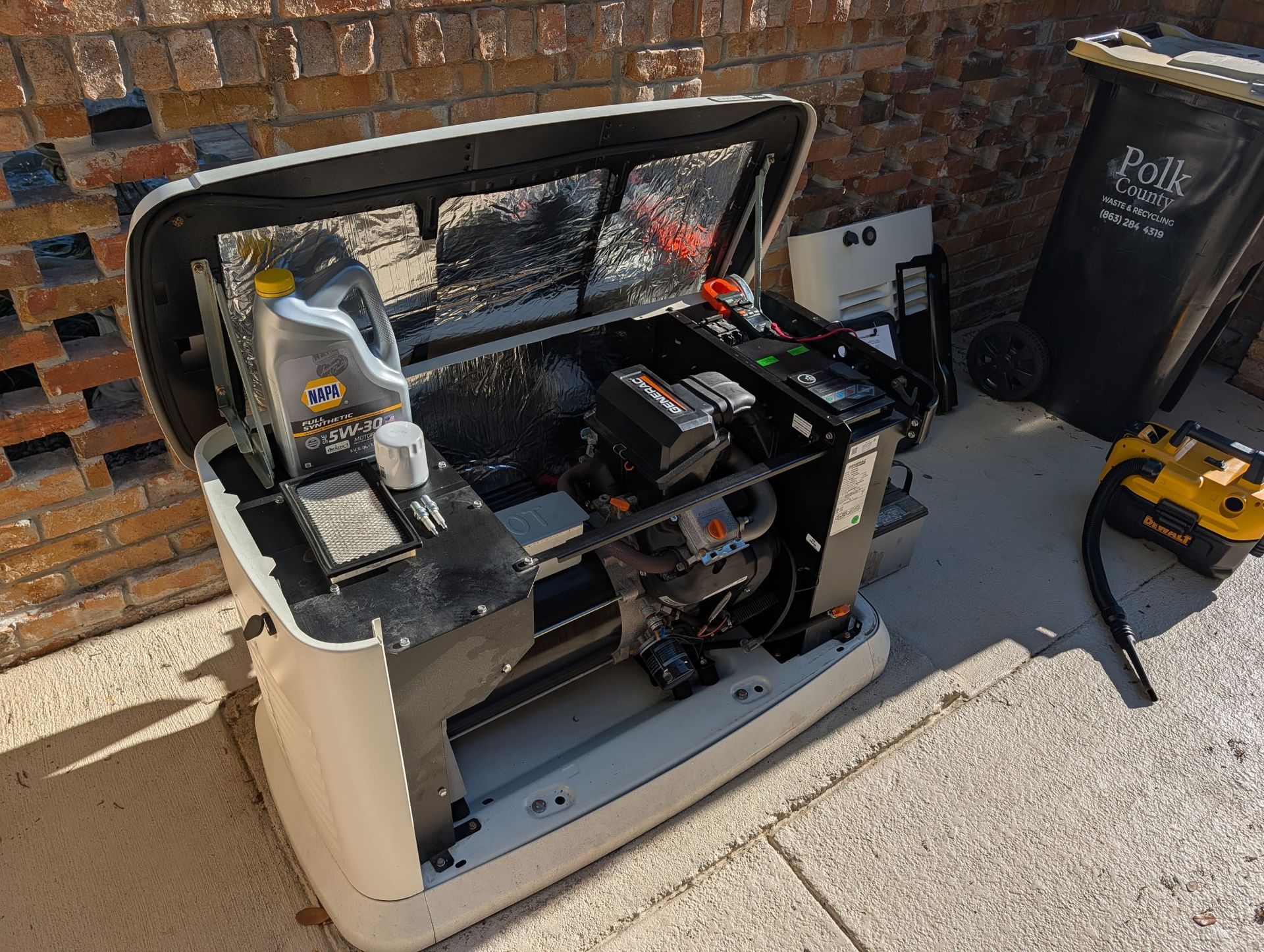 AC unit and generator near a beige house with red roof and green lawn.