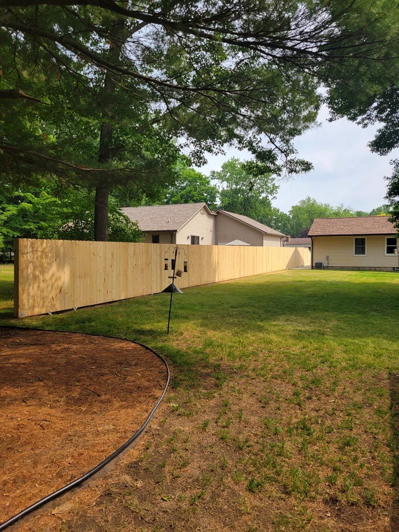 Wooden fence in a backyard; grass, trees, and houses in the background.