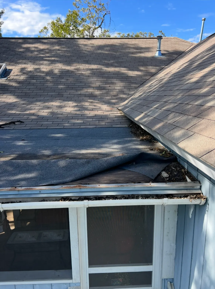 Damaged roof with torn shingles and a collapsed section above a screened porch
