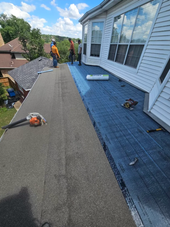 Roofers installing shingles on a steep house roof, with tools and materials spread across the roof.