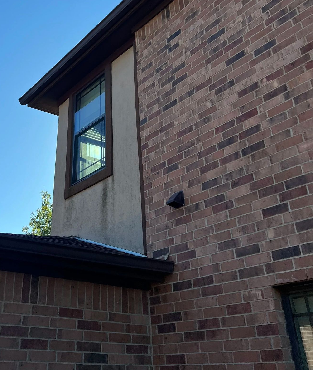Brick house exterior with tan siding, dark roof trim, and a window against a blue sky
