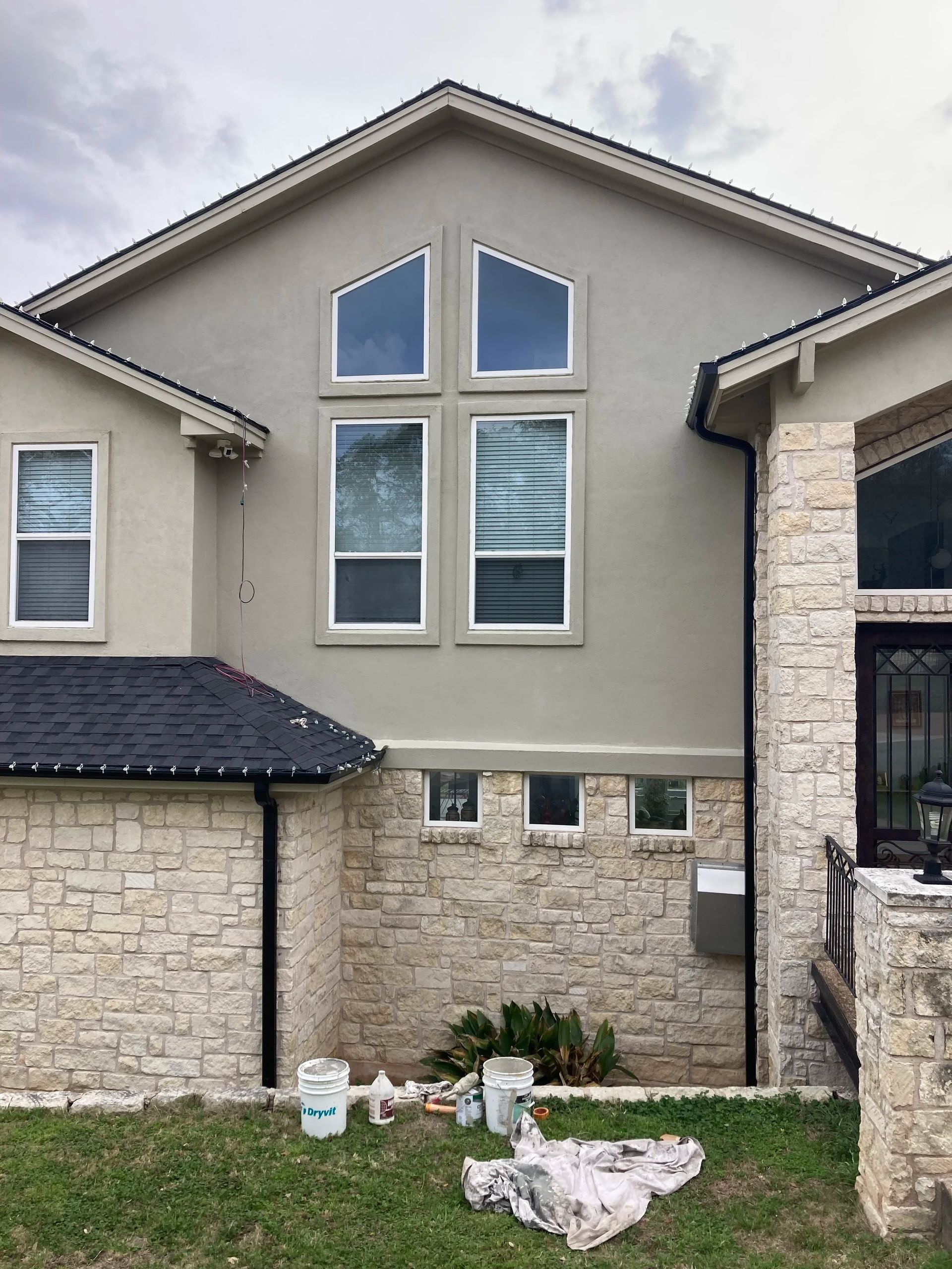 Modern beige stone-and-stucco house exterior with large windows and a small grassy front yard.
