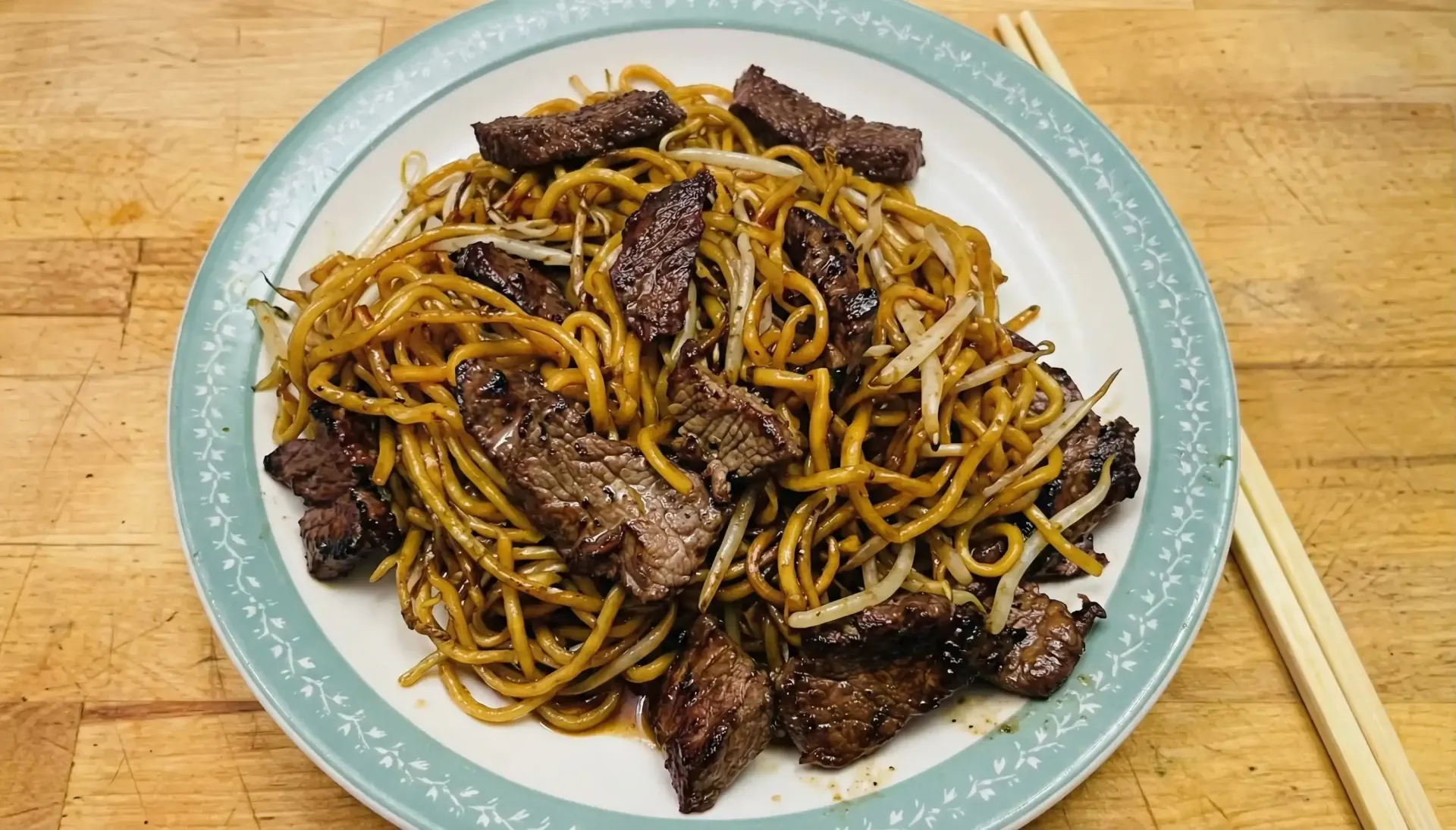 Plate of noodles and beef with bean sprouts, chopsticks alongside.