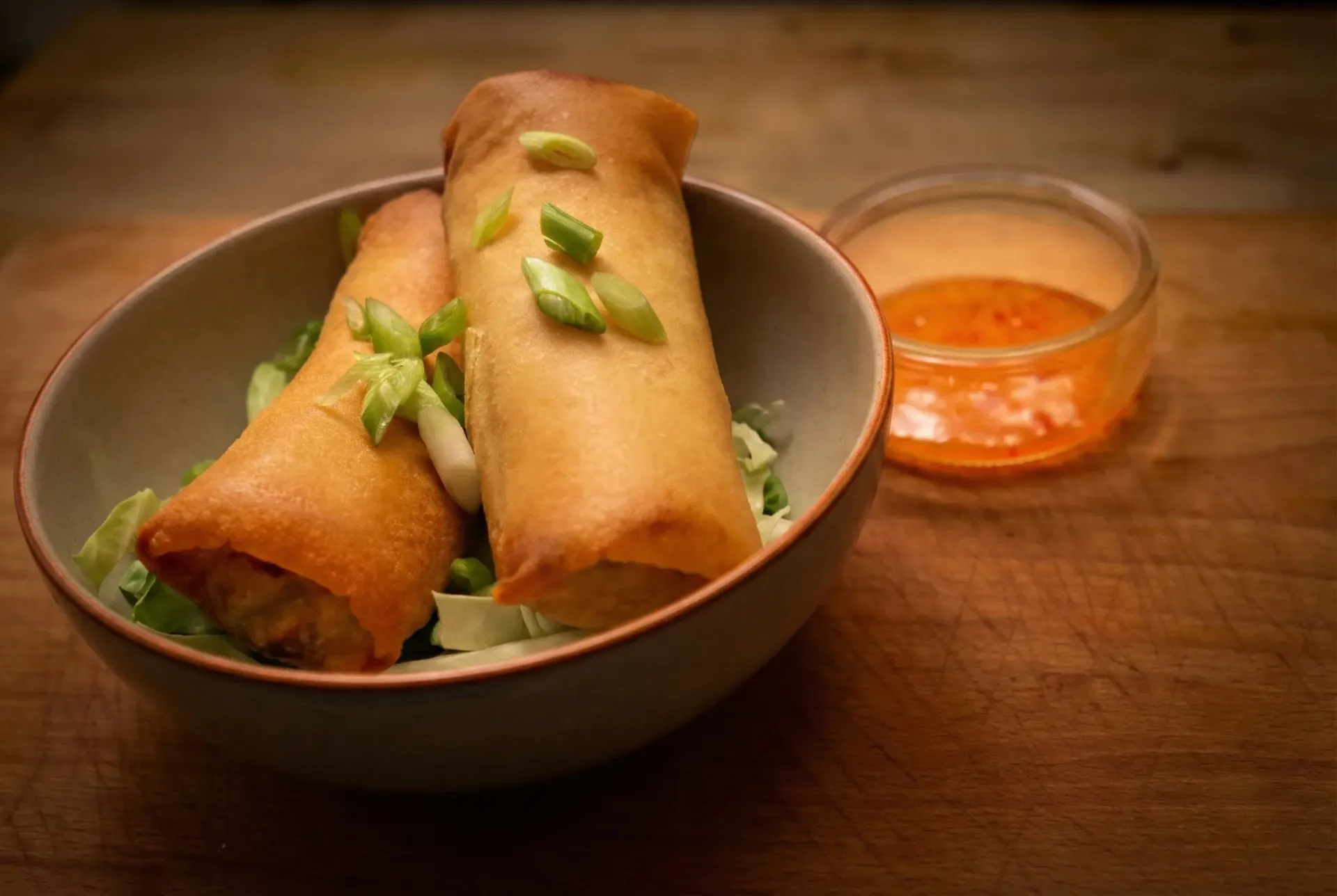 Two golden spring rolls on a white plate, garnished with mint, with a brown stripe design.