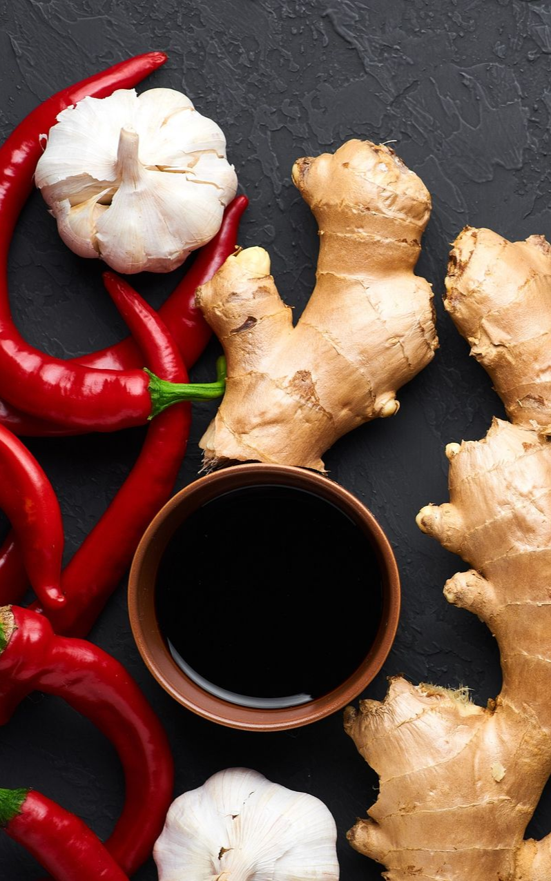Red chilies, garlic, ginger, and soy sauce in a bowl on dark surface.