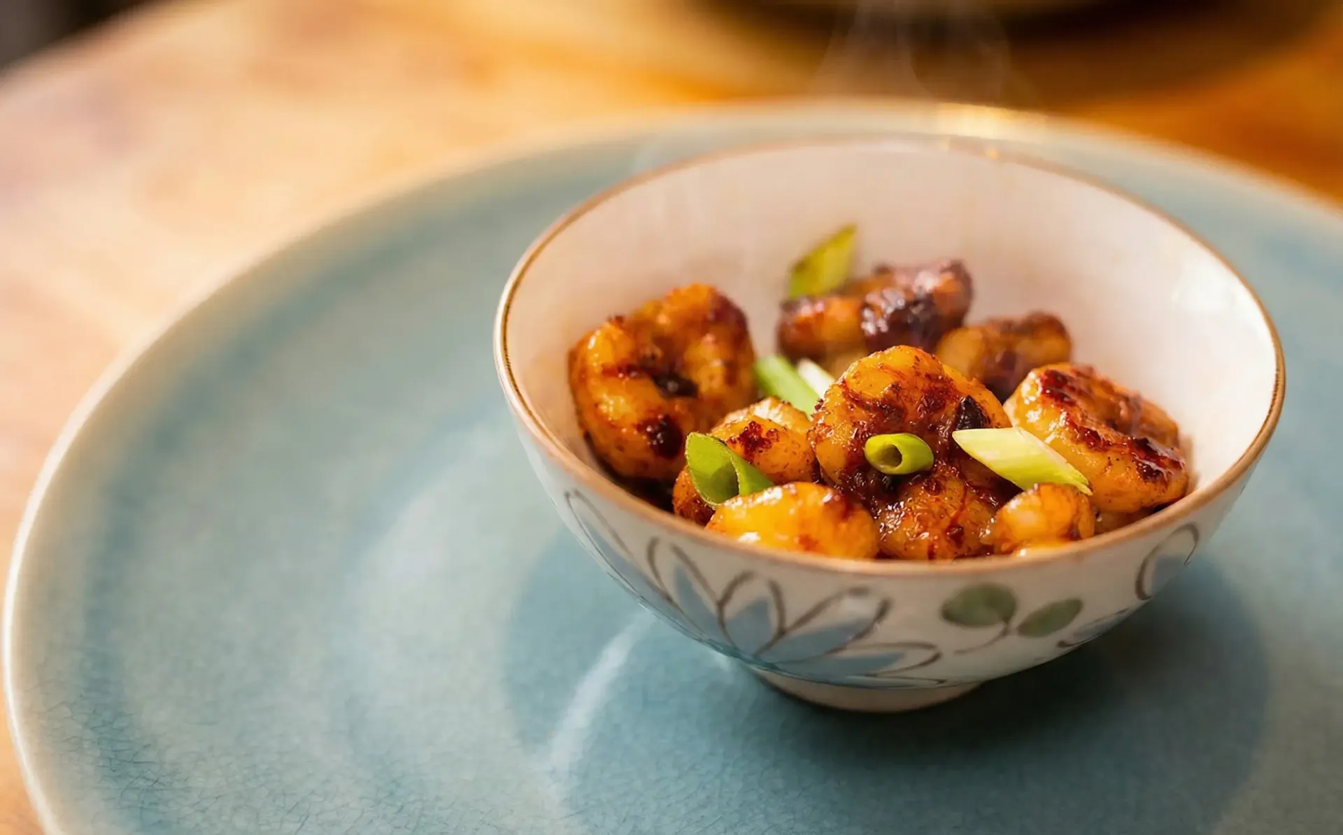 Bowl of glazed shrimp with green onions on a blue plate, close up.