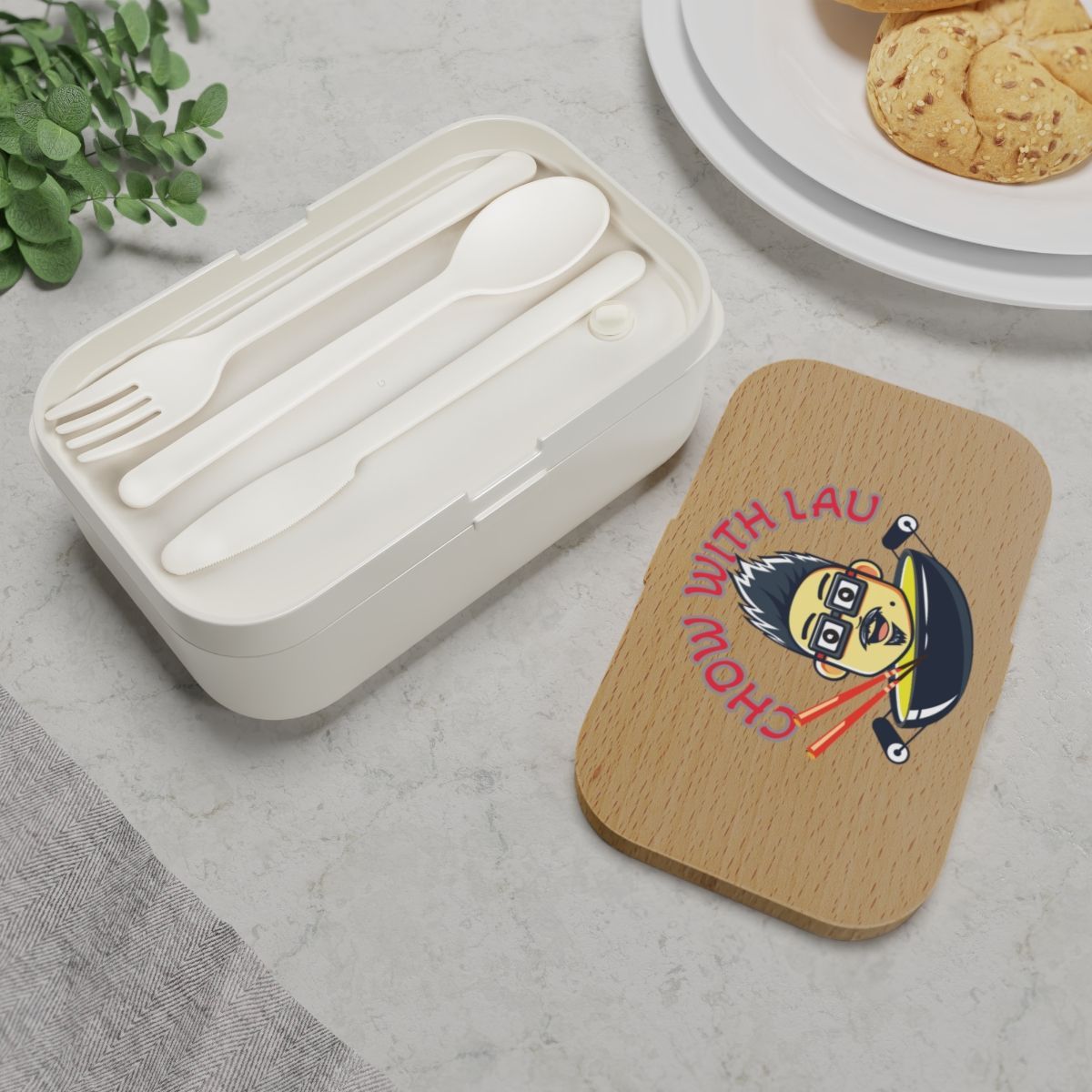 Lunchbox with utensils and a lid featuring a cartoon eating noodles.