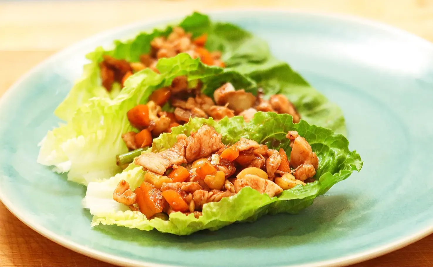 Cooked shrimp in orange sauce, held with chopsticks, in a black bowl.