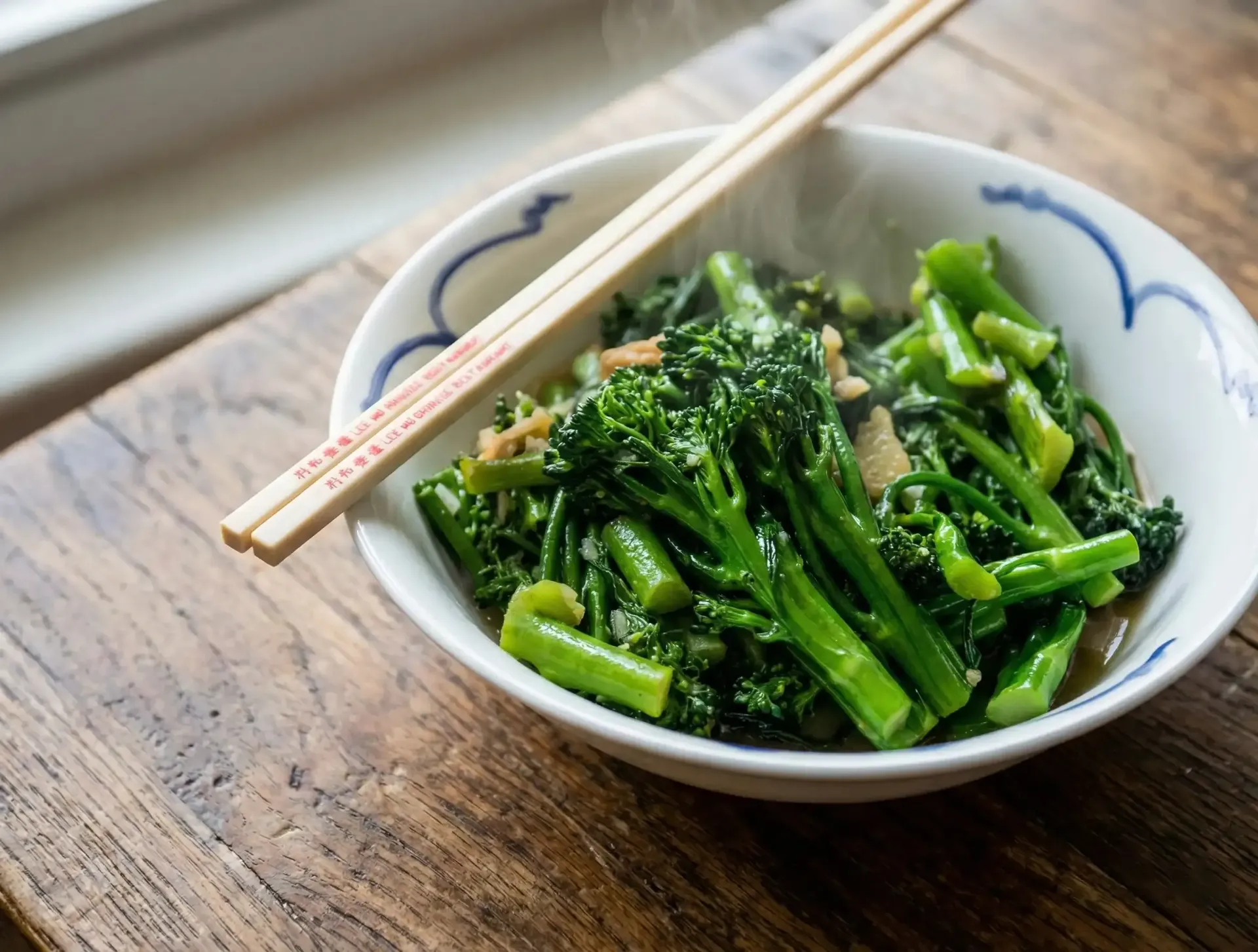 Bowl of steamed green vegetables with chopsticks on wooden table.
