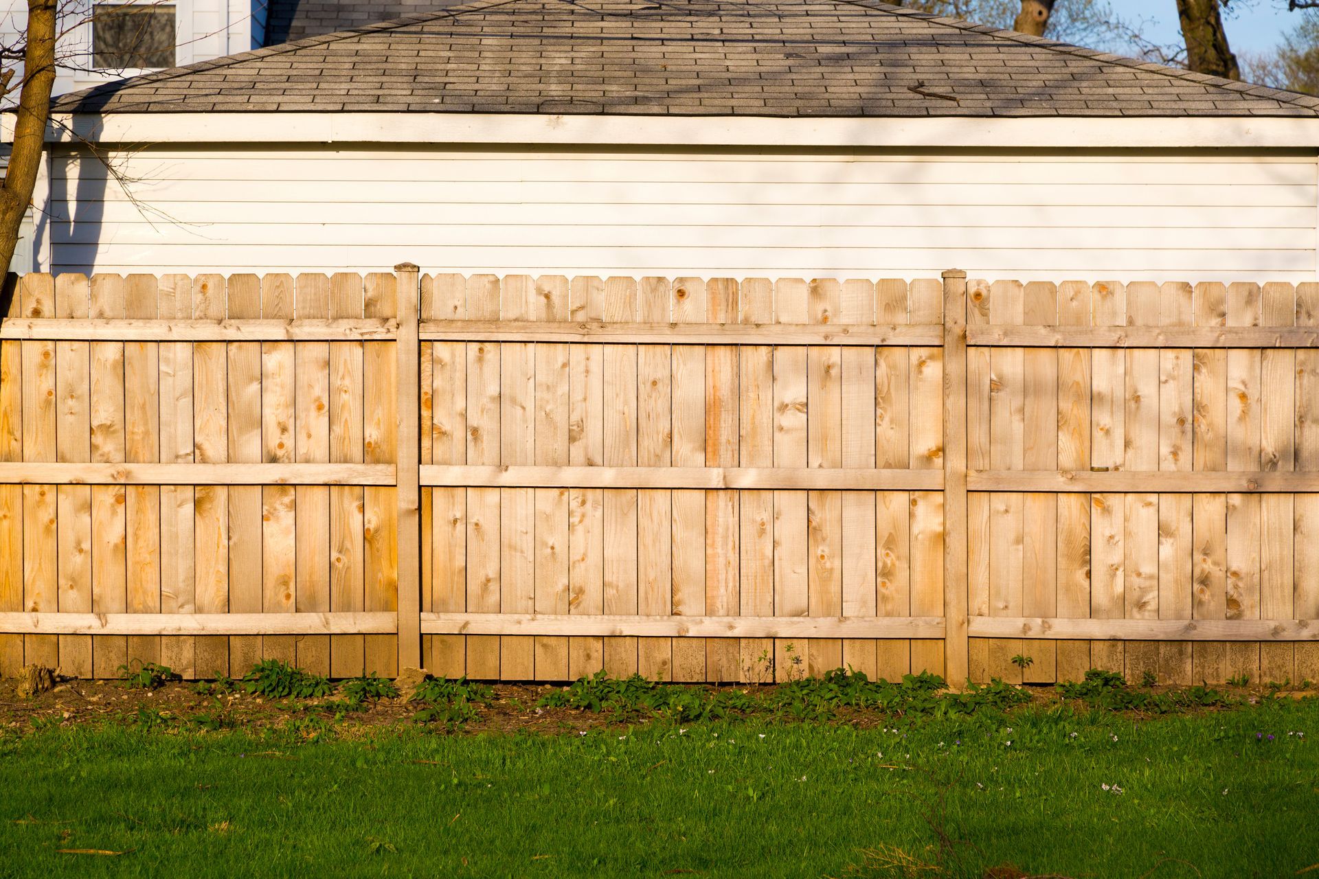Wooden privacy fence with white garage wall behind it and grass in front