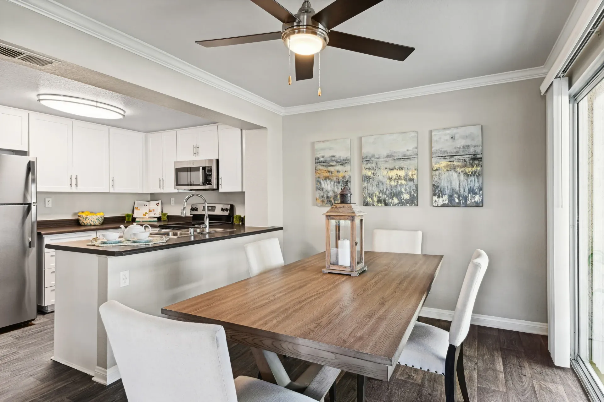 Open-plan kitchen and dining area with white cabinets, stainless steel appliances, and a wooden dining table.