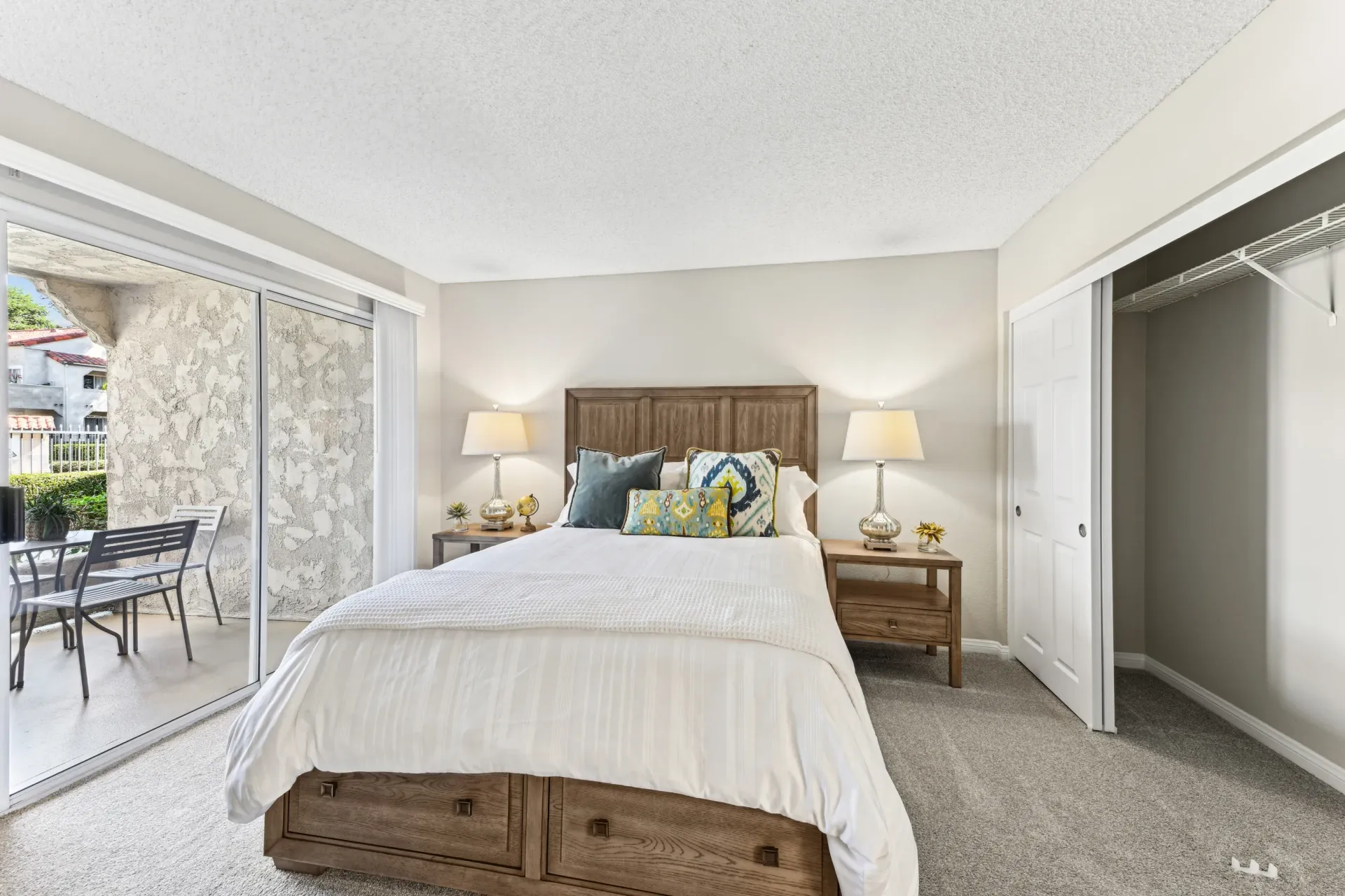 Bedroom in an apartment with a wooden bed, two nightstands, and a sliding glass door to a balcony.