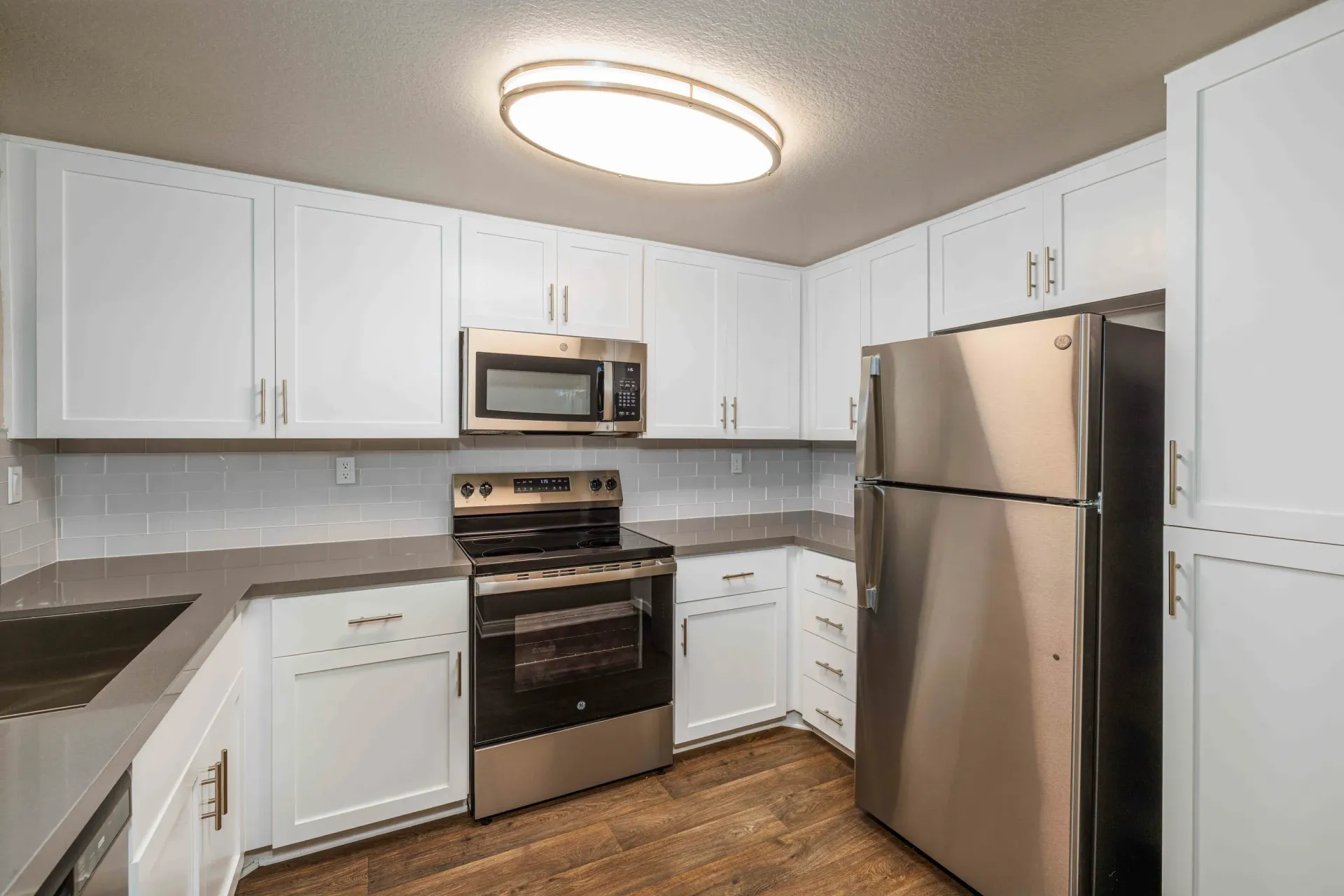 White kitchen with stainless steel fridge, oven, microwave, and white cabinets.