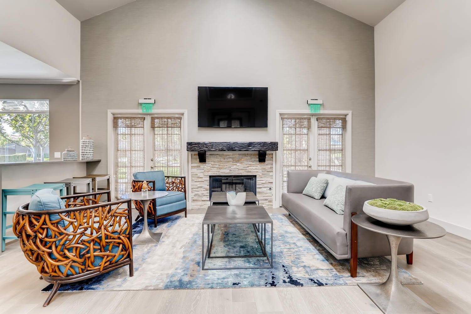 Contemporary communal living area with gray sofa, blue chairs, stone fireplace, wall-mounted TV, and glass doors.