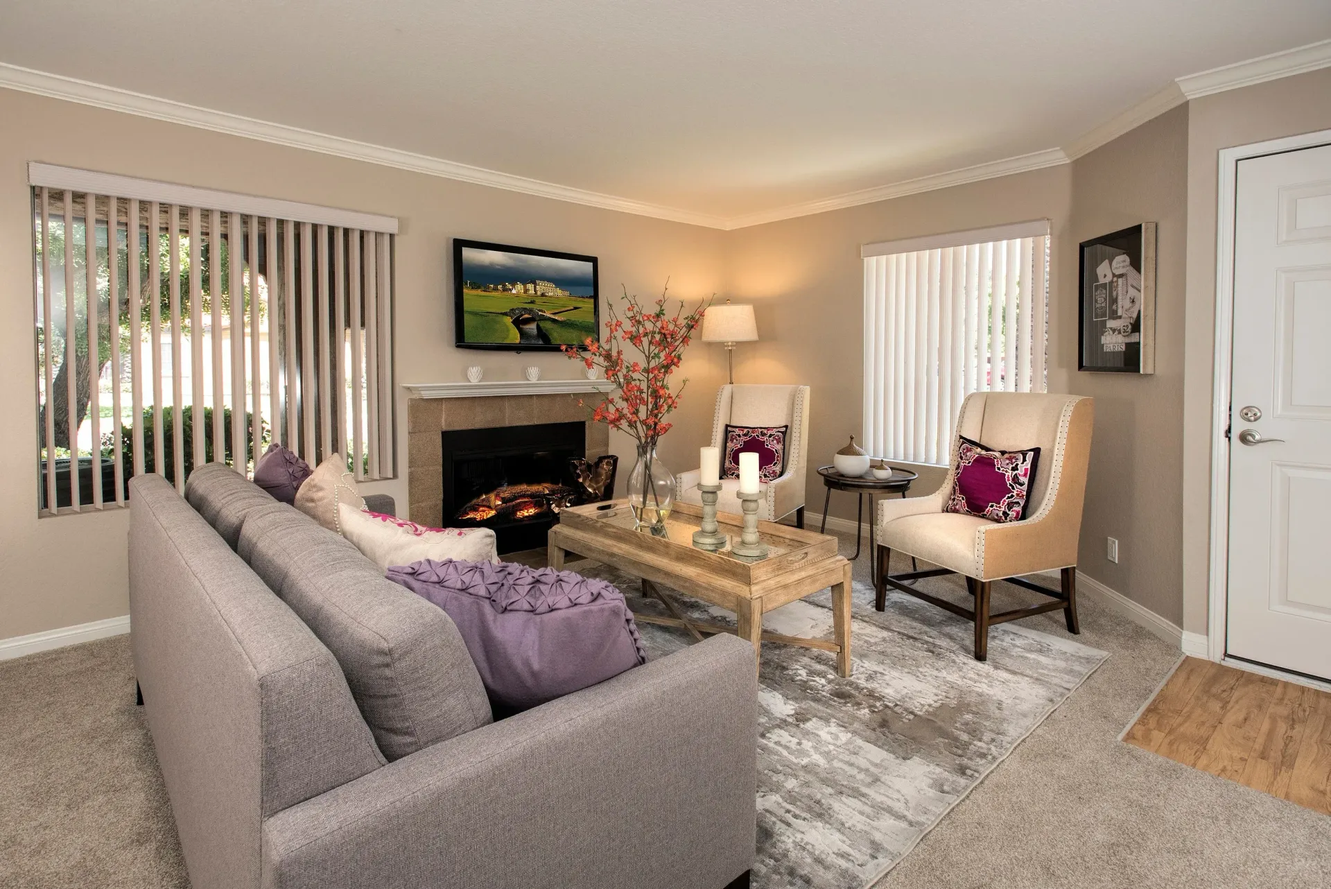 Living room in a neutral apartment with a fireplace, TV, sofa, and two armchairs.