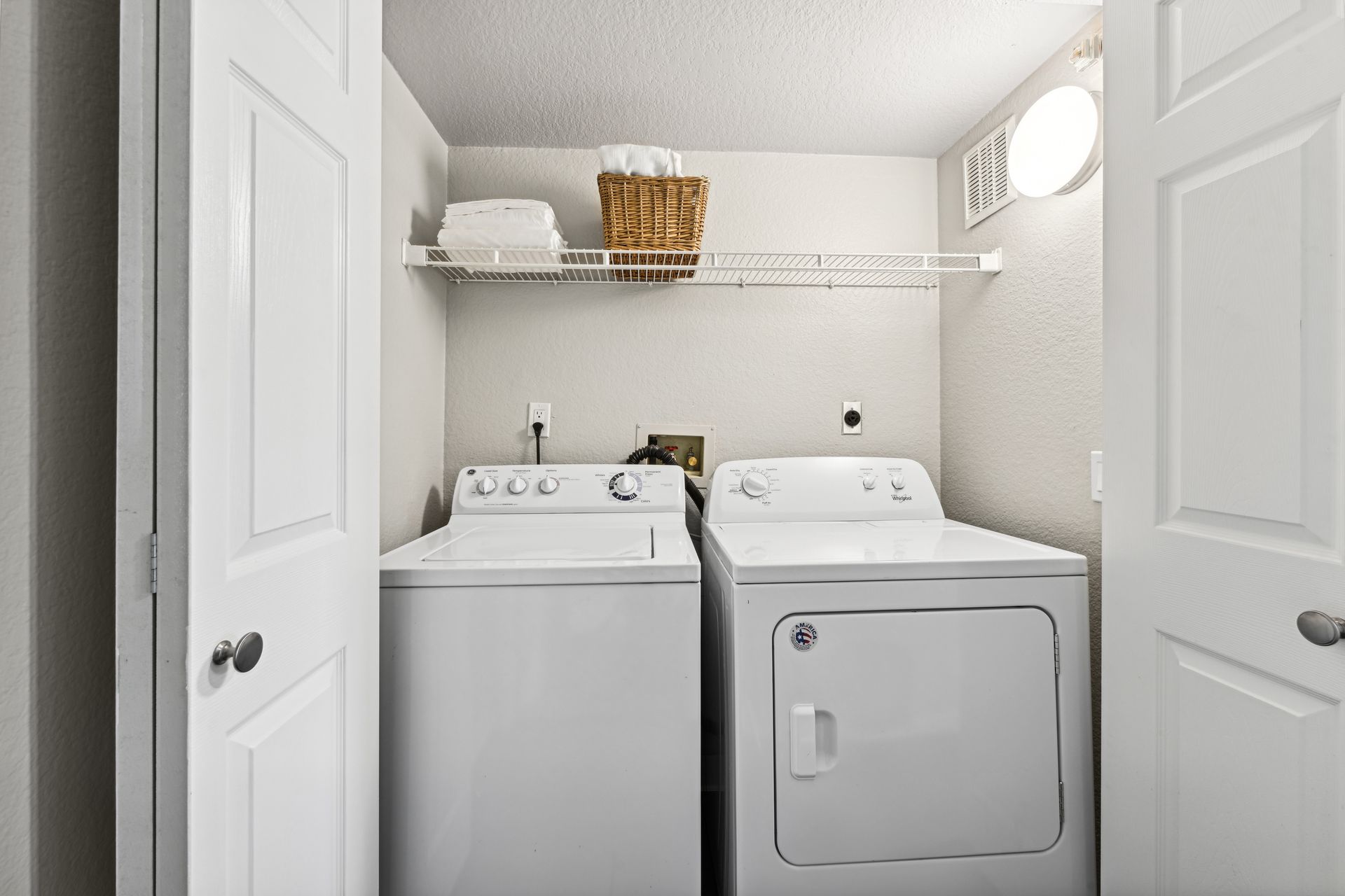 Laundry room with white washer and dryer, shelf with basket, white doors.