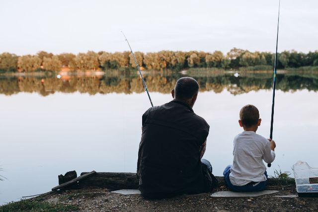 A man and a boy are sitting on a dock fishing in a lake.