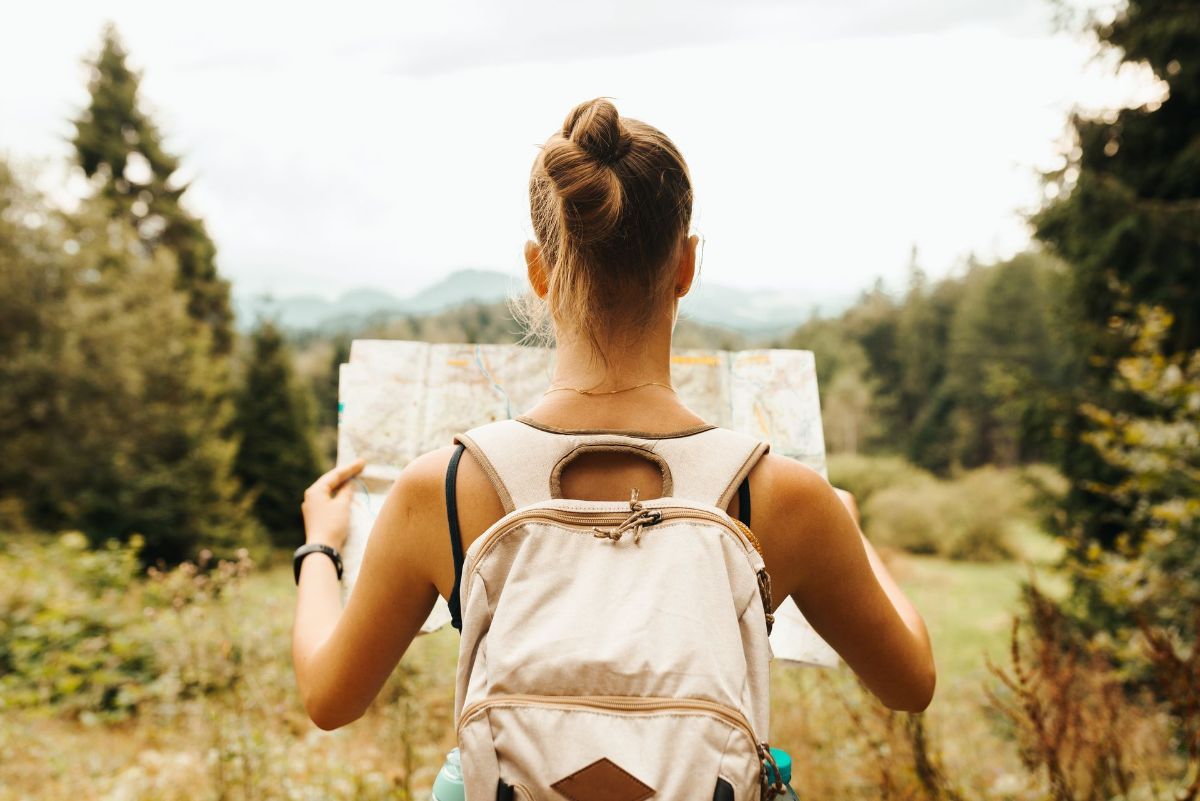 A woman with a backpack is looking at a map in the woods.