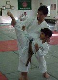 Man assisting a child in a high kick exercise during a karate class.
