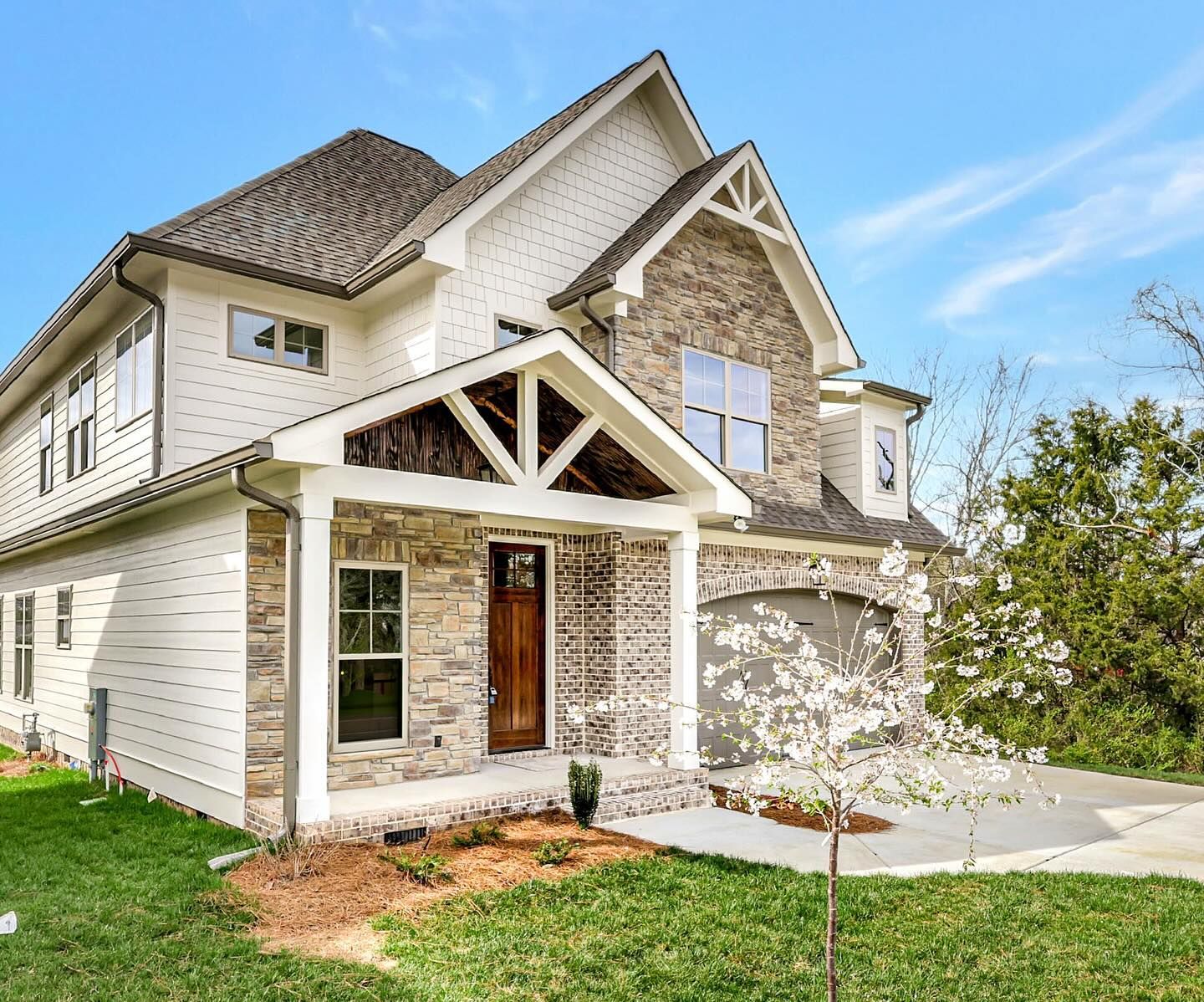 Two-story house with white siding, stone accents, and brown front door on a sunny day.