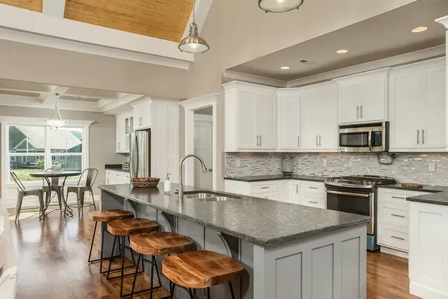 A kitchen with white cabinets , granite counter tops , stainless steel appliances and a large island.