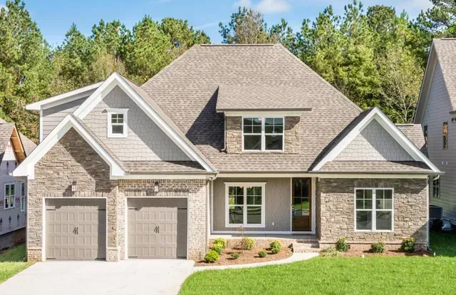 A large brick house with a gray roof and two garages is sitting on top of a lush green lawn.