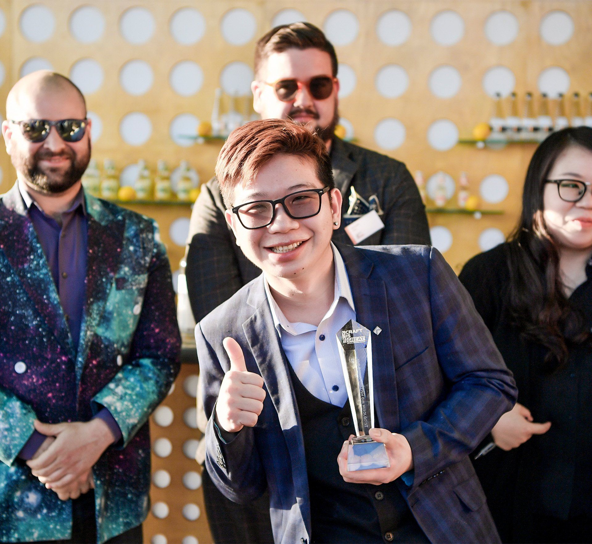 A man in a suit and glasses is giving a thumbs up