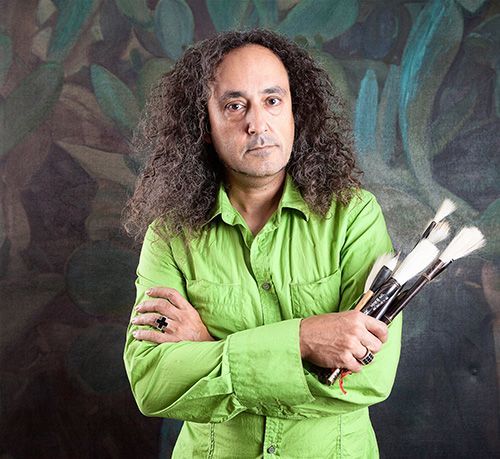 A man with long curly hair is holding a bunch of brushes