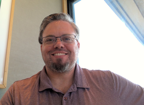 Business team, woman with crossed arms smiling in front. People in suits, office setting.