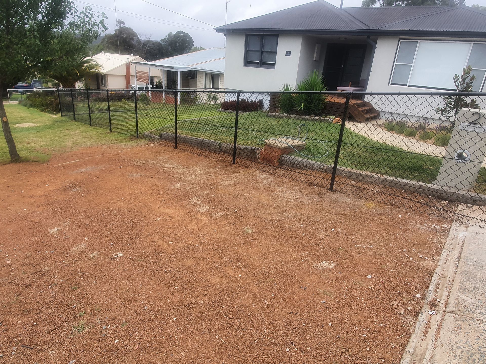 A Black Fence Is Surrounded by Trees and Bushes in A Backyard — GnB Fencing and Excavation in Queanbeyan, NSW