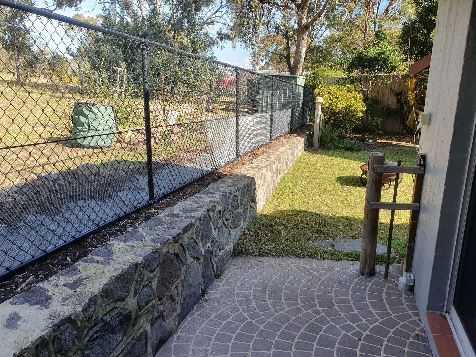 A Fence Surrounds a Lush Green Yard Next to A House — GnB Fencing and Excavation in Queanbeyan, NSW