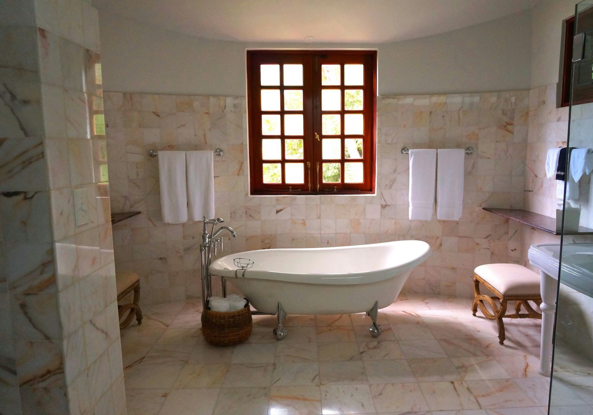 Bathroom with a claw-foot tub, a window, and marble walls and floors. Two towel racks hold white towels.