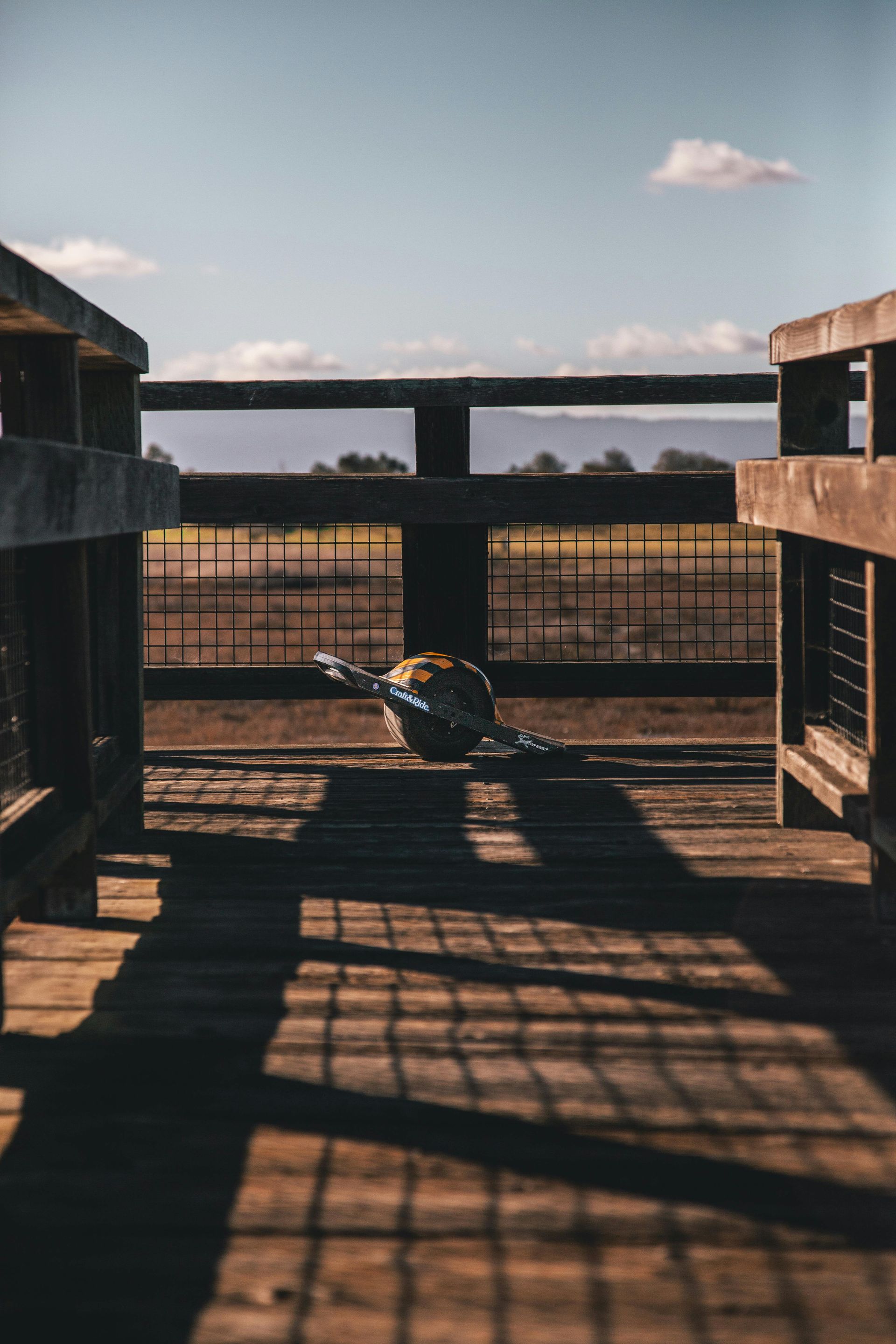 Wooden bridge overlooking a field, shadows cast by railing and a centered object.