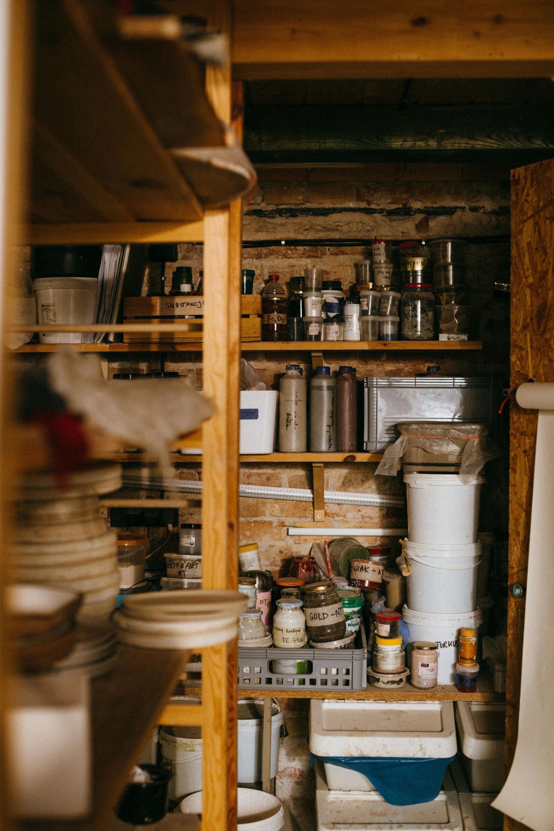 Shelves filled with pottery supplies in a rustic workshop. Jars, canisters, and containers line the shelves.
