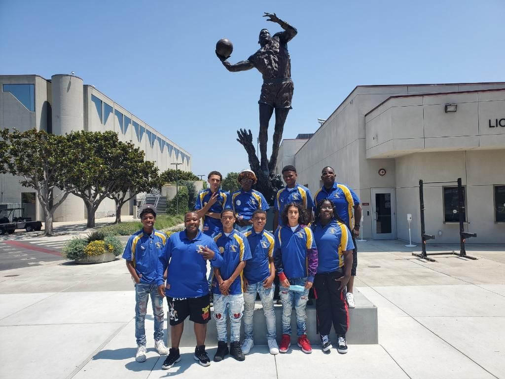 A group of people standing in front of a statue of a man holding a basketball.