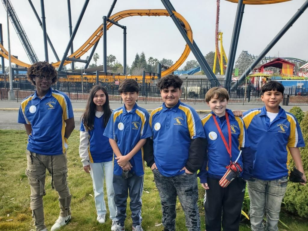 A group of young people are posing for a picture in front of a roller coaster.
