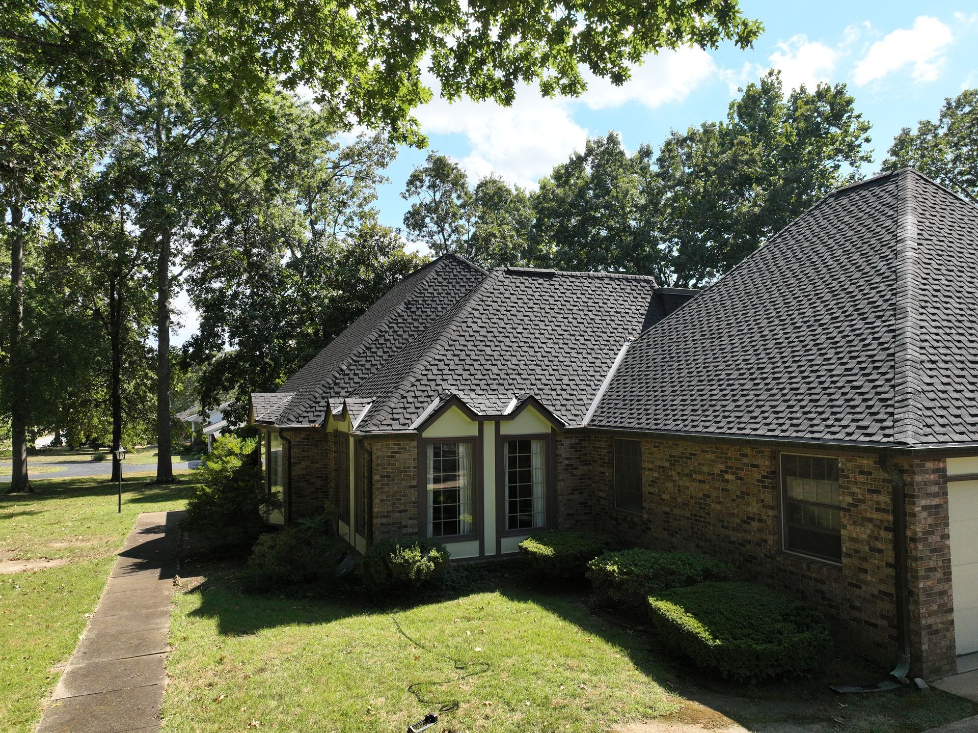 Brick ranch house with green metal roof, white garage door, and a person working outside.