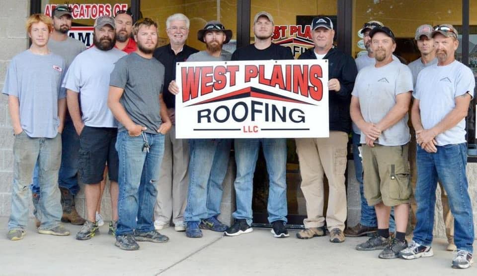 A group of men from West Plains Roofing, LLC, pose with a sign outside a building.