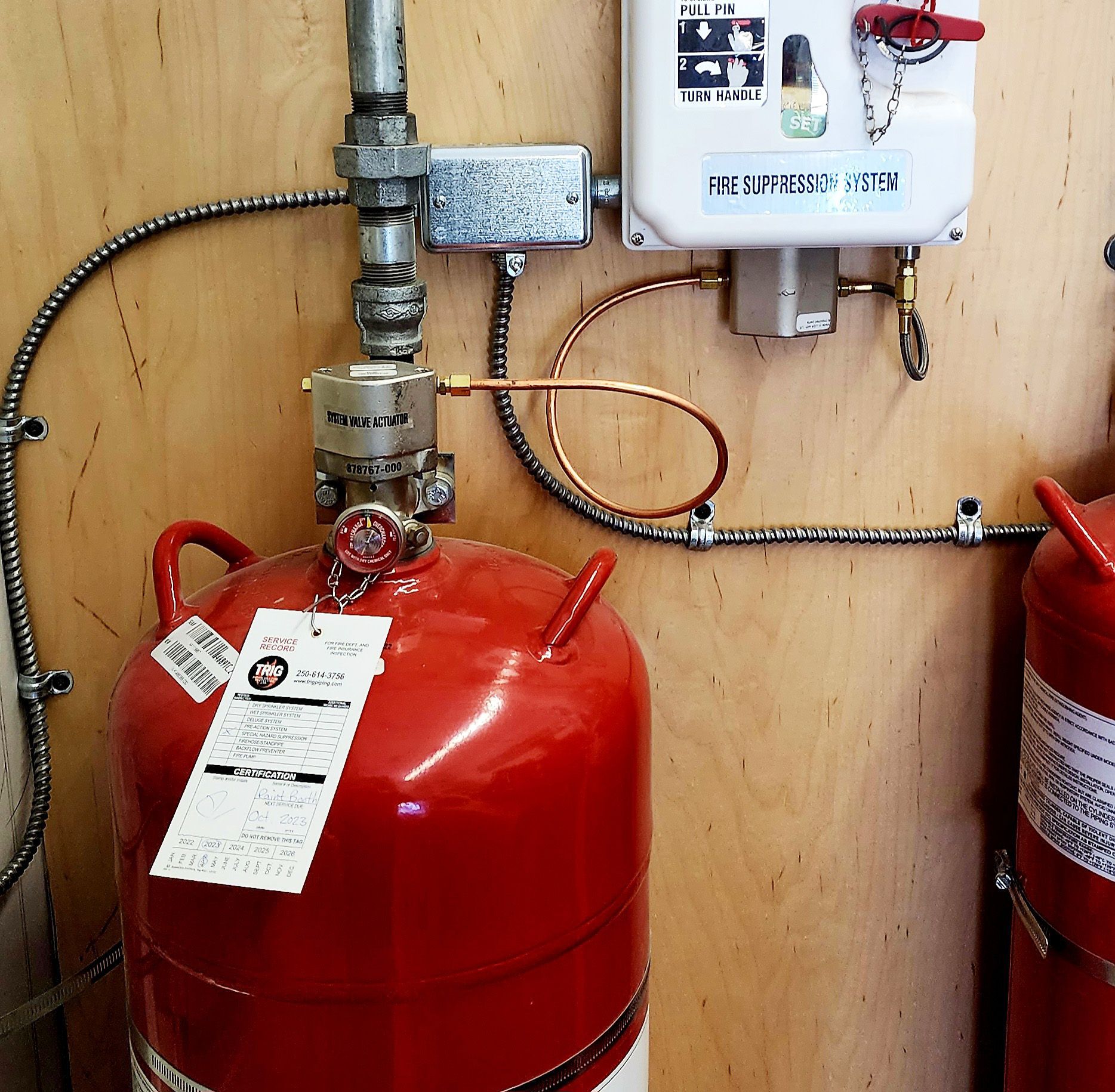 Red fire suppression system tanks mounted on a wall with pipes and a control box.