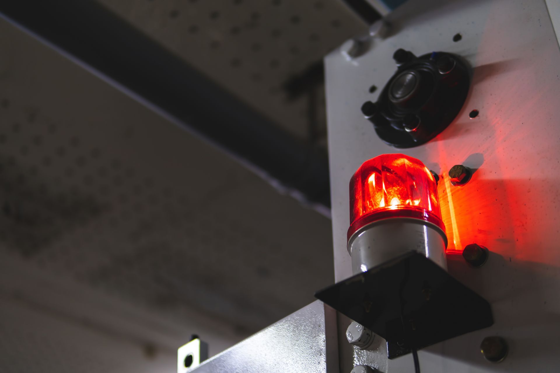 A bright red warning beacon light illuminates a gray industrial control panel in a dark setting.
