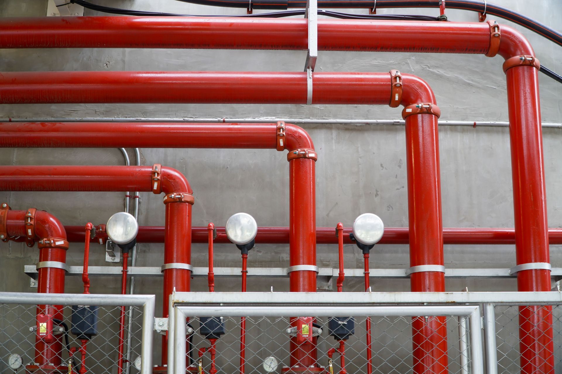 Red fire suppression pipes with gauges, mounted on a wall.