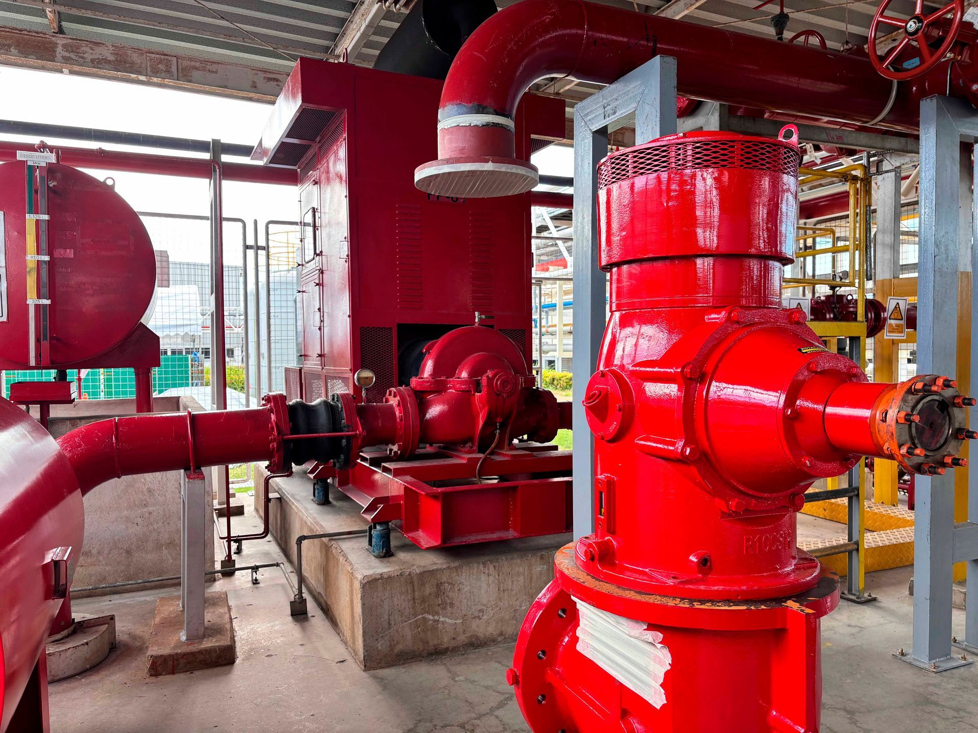 Red fire pump system with pipes and a hydrant in an industrial setting.