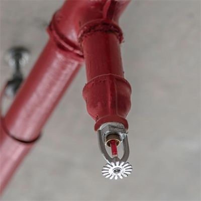 Red fire sprinkler head attached to a red pipe, mounted on a gray ceiling.