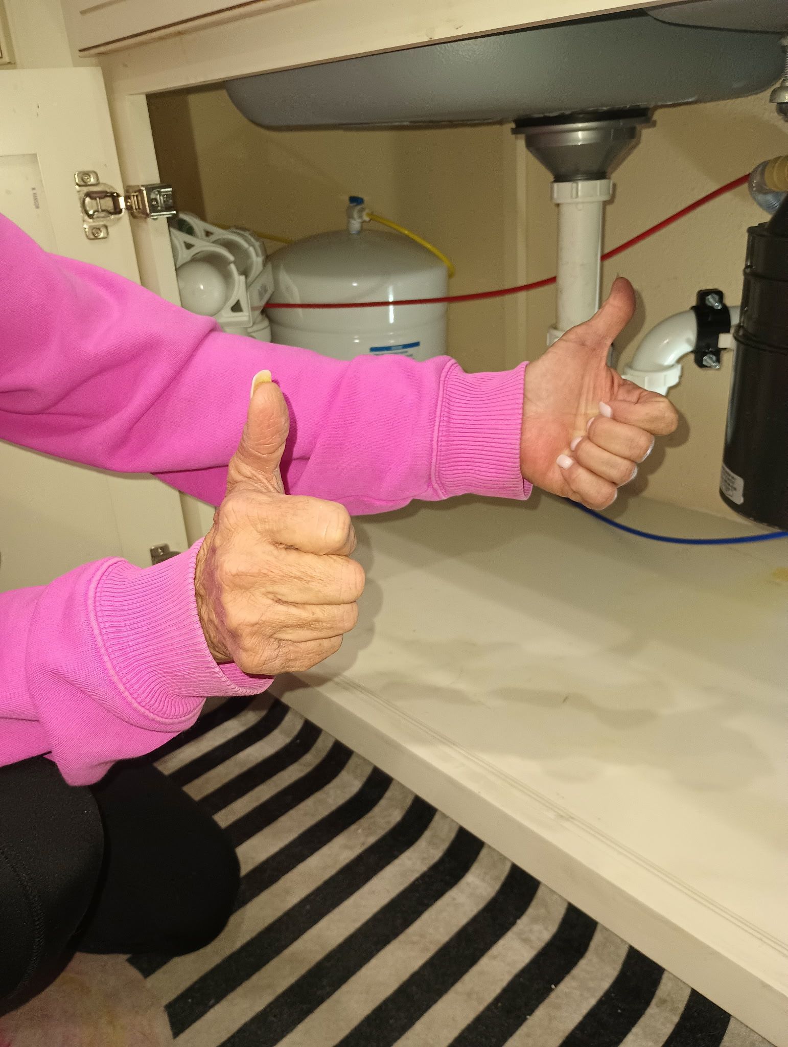 Person giving two thumbs up under a kitchen sink with a water filtration system.