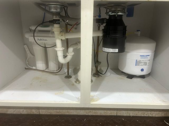 Underside of a kitchen sink cabinet: a water filter, garbage disposal