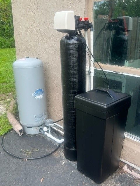 Water softener system outdoors, gray tank, tall black tank, and black salt container.