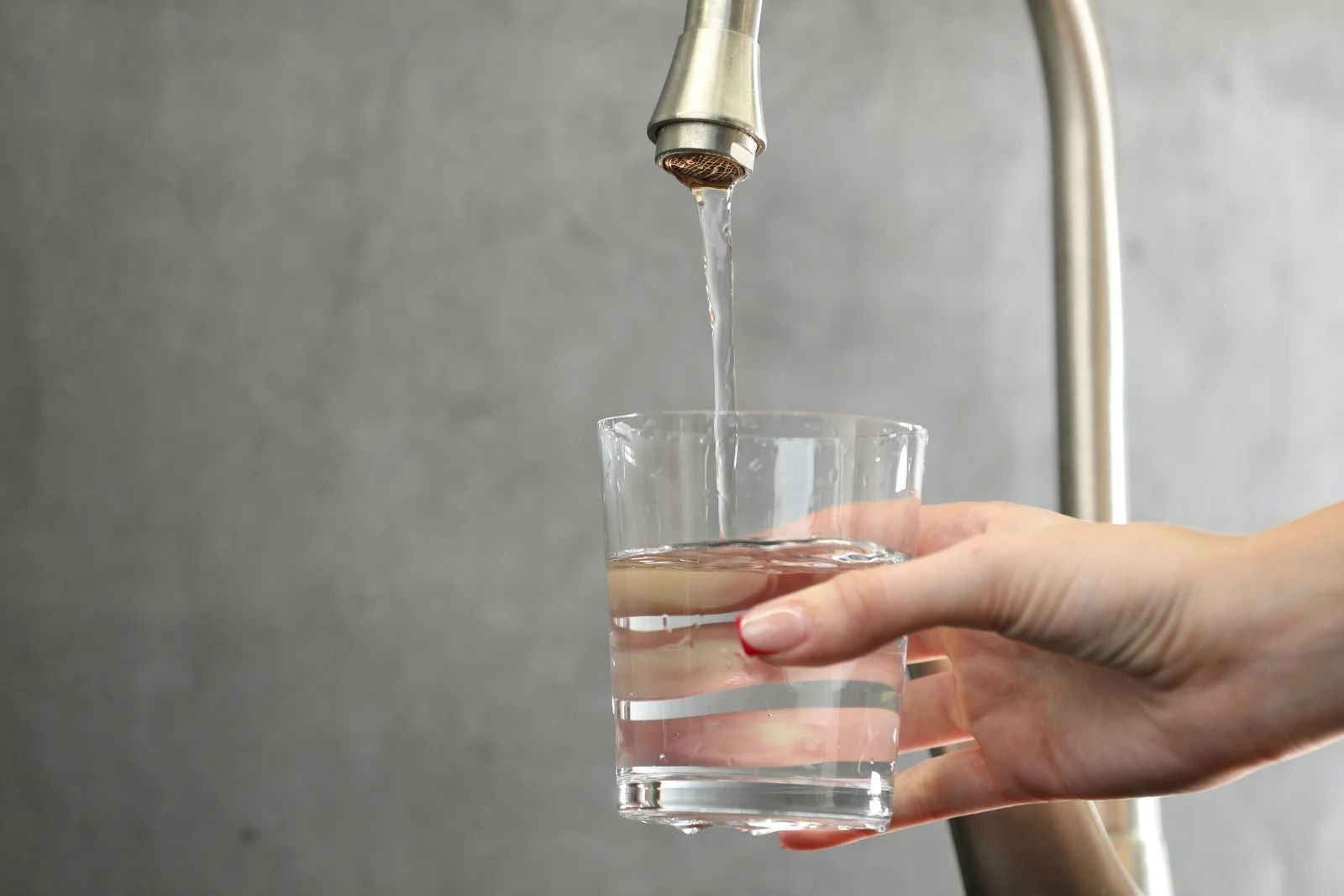 A hand holds a clear glass under a kitchen faucet as water pours into it.
