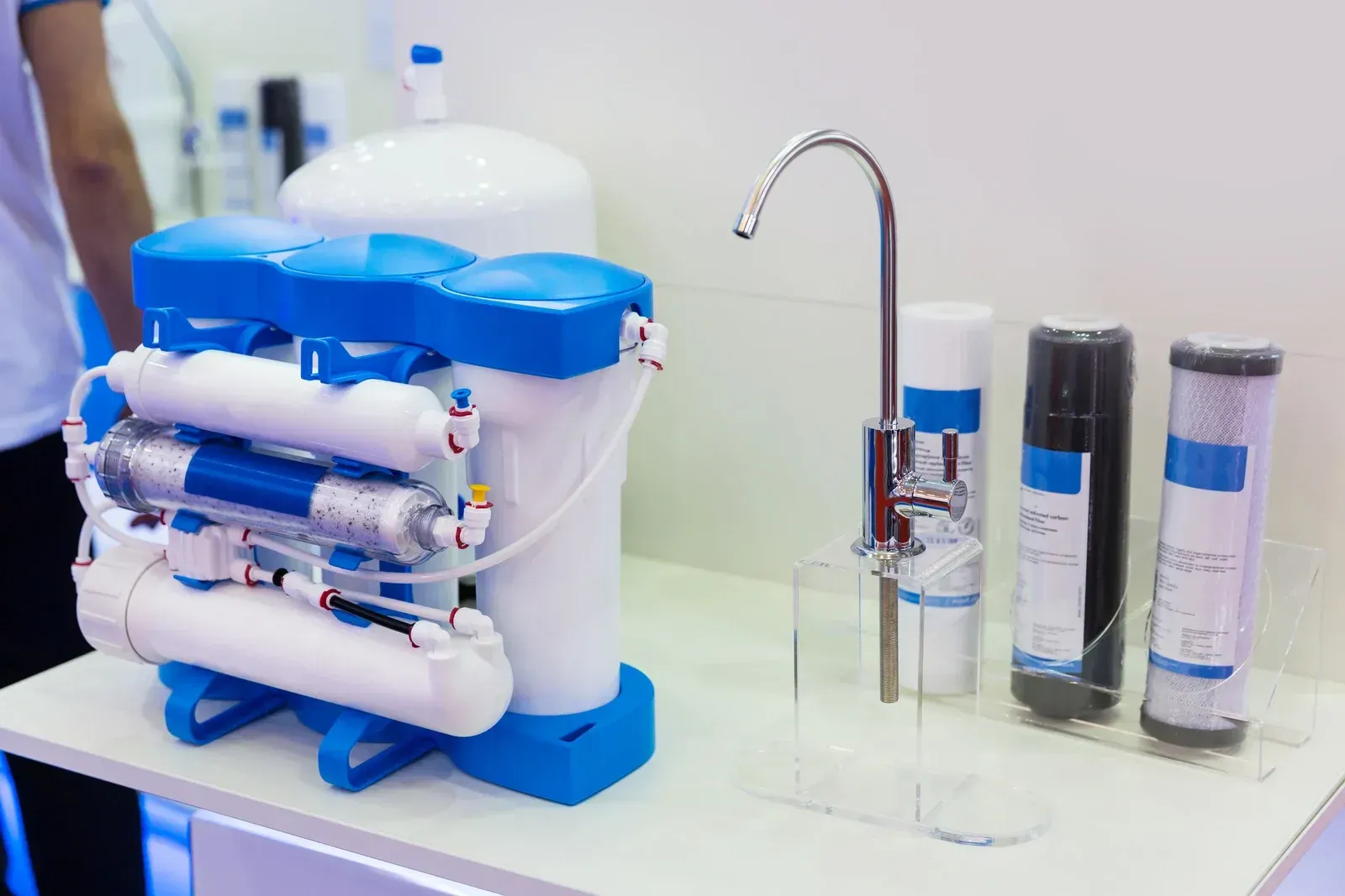 Compact water purifier with blue and white filters next to a chrome faucet and cartridges on a countertop